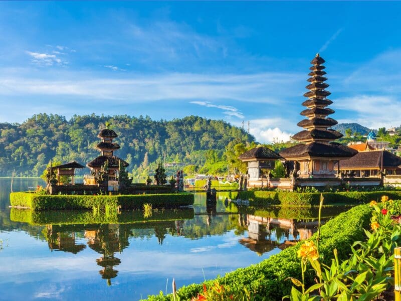 Scenic view of a traditional Balinese temple with water reflections and lush hills. Scenic view of a traditional Balinese temple with water reflections and lush hills.